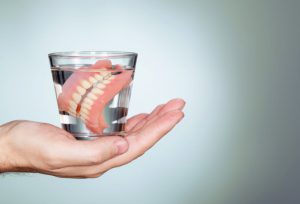 hand holding a cup of water with dentures soaking in it